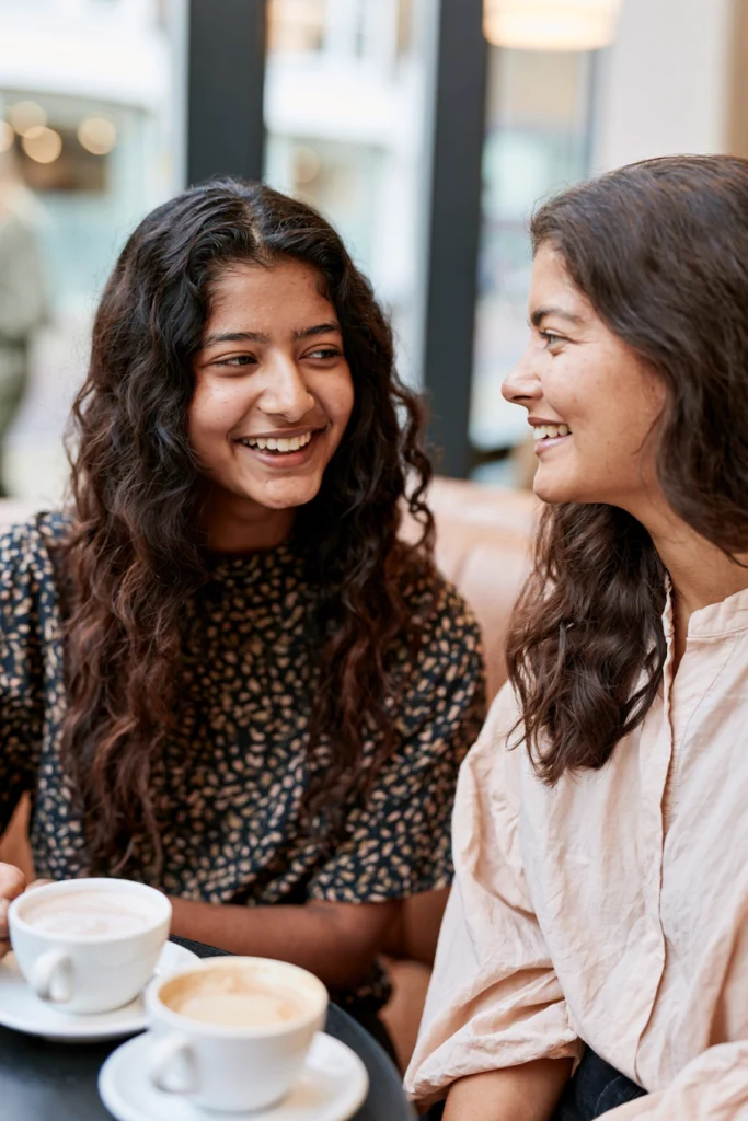 A mother and an autistic teenage girl sit together chatting in a cafe.