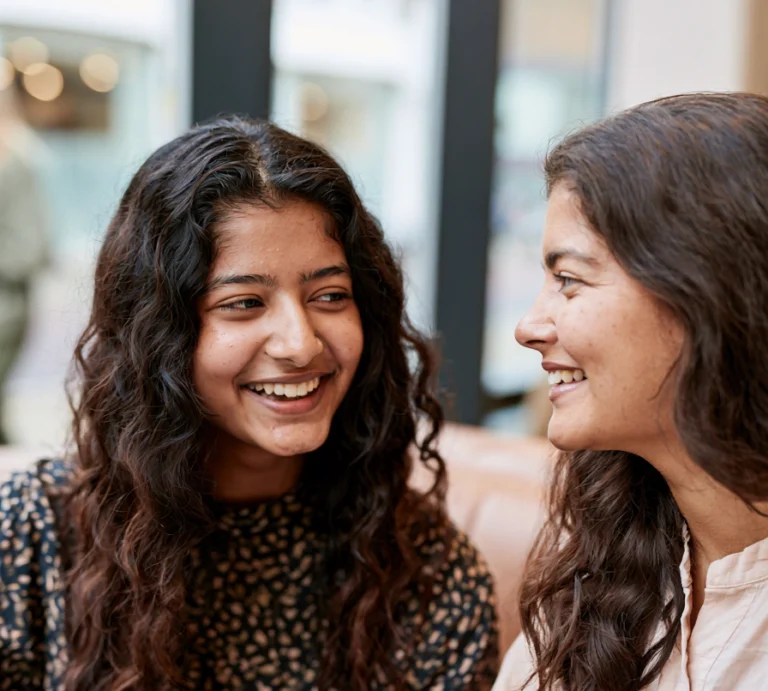 A mother and an autistic teenage girl sit together chatting in a cafe.