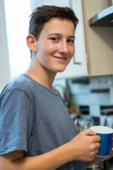 An autistic teenage boy in his kitchen holding a mug of tea.