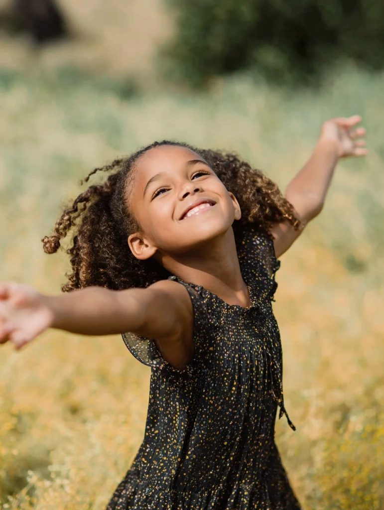 A little girl of about seven years old, with her arms outstretched as though she is dancing, in a field.