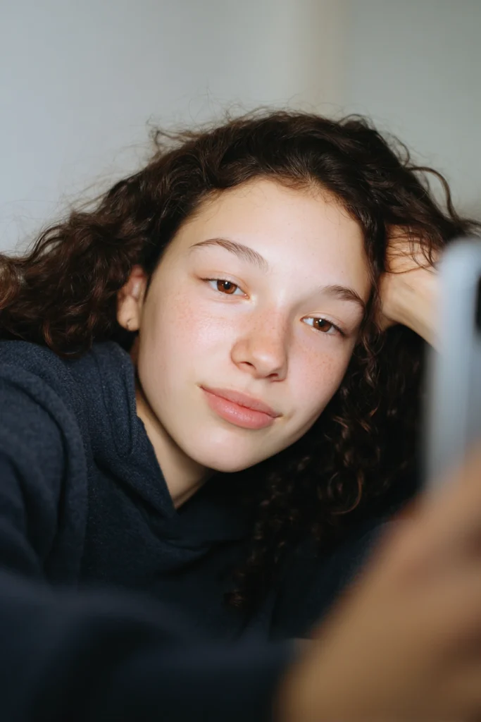 A thoughtful 16-year-old girl wearing casual clothing, sitting on a sofa and resting her head on her arm.