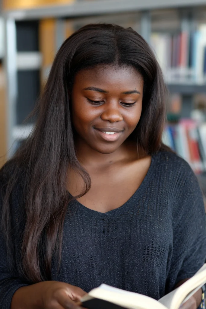 A sixteen-year-old girl in a library reading a book whilst standing