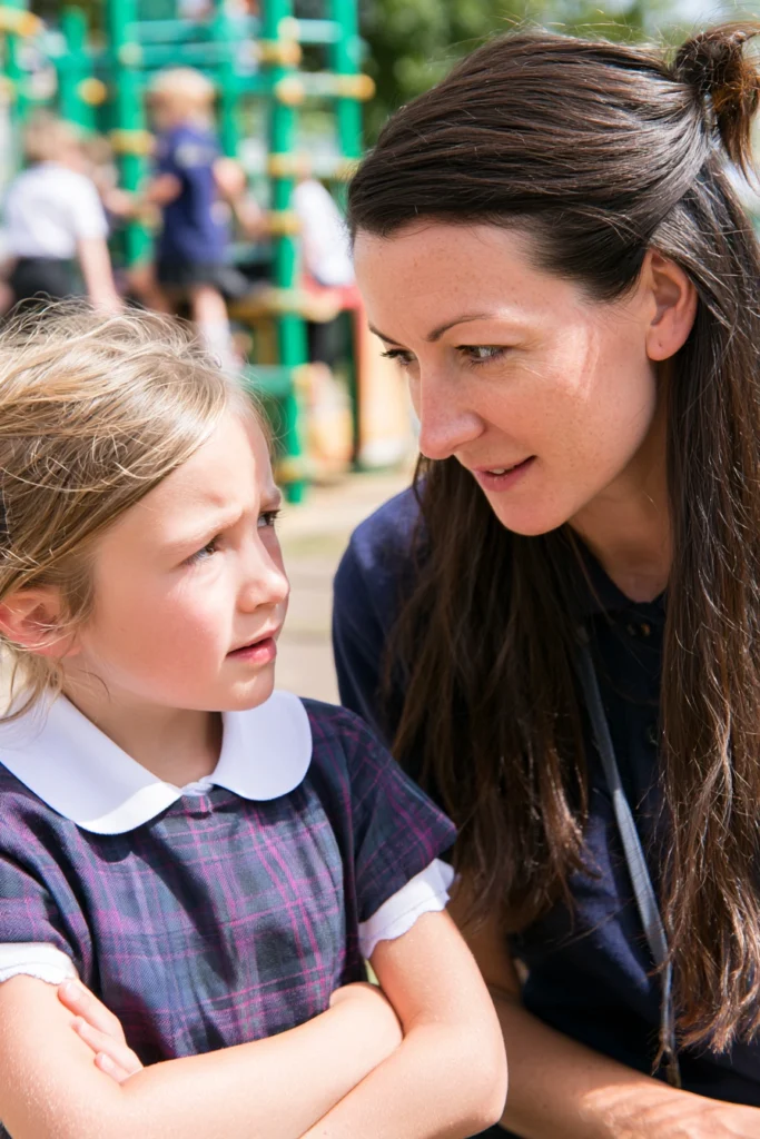 An anxious elementary school child talking to her teacher in the school yard