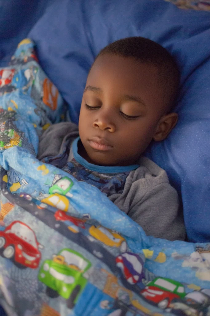 A little boy of about five years old, sleeping soundly on a blue pillow with a cars duvet