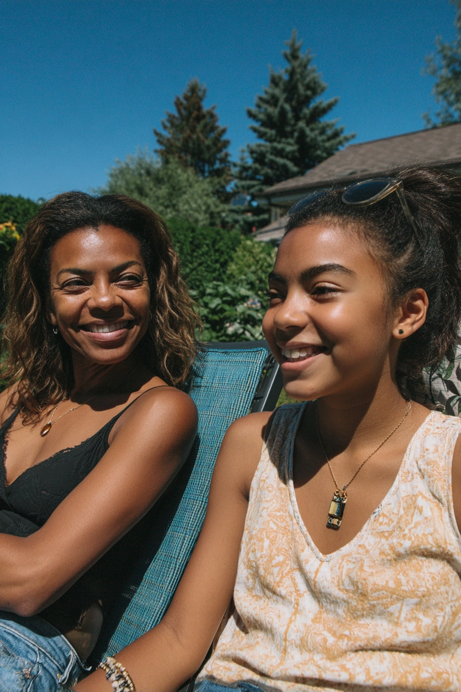 A happy teenage girl and her mother sit on sun beds in a sunny garden.