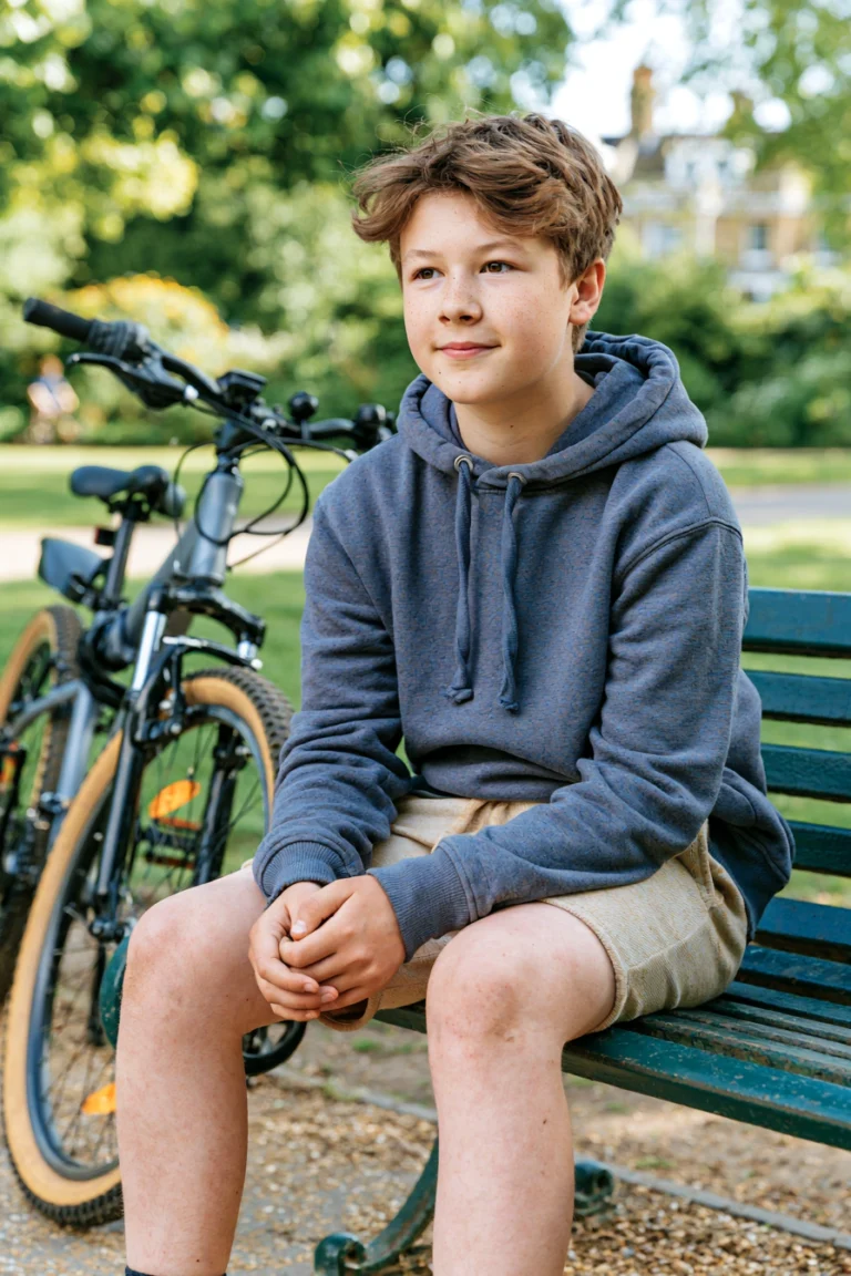 A teenage boy sitting in a park with his bike resting against the bench