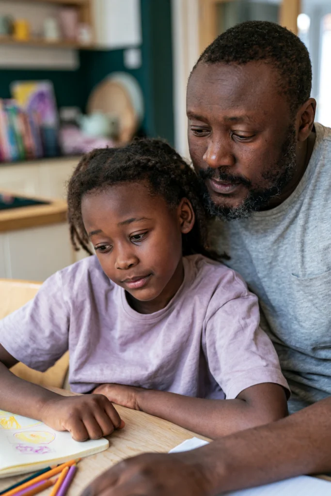 A father and seven-year-old daughter sitting at their kitchen table drawing together