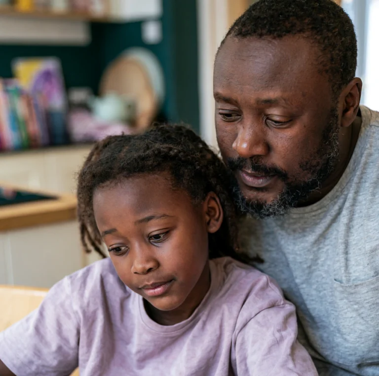 A father and seven-year-old daughter sitting at their kitchen table drawing together