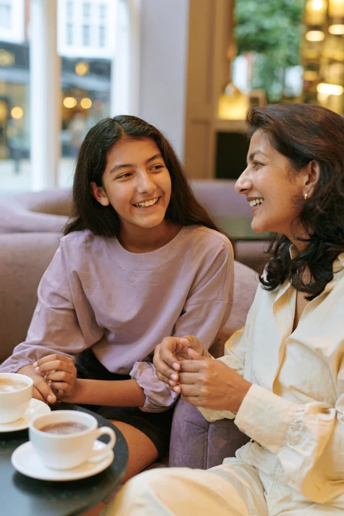 A happy teenage girl sits with her mother in a cafe.