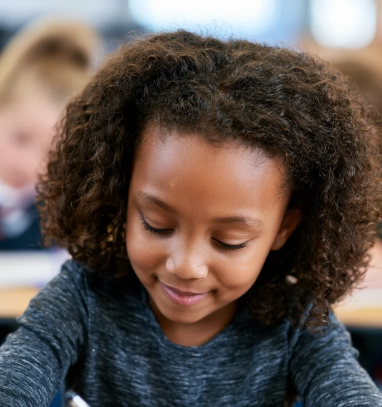A happy little girl writing at a desk in a school classroom